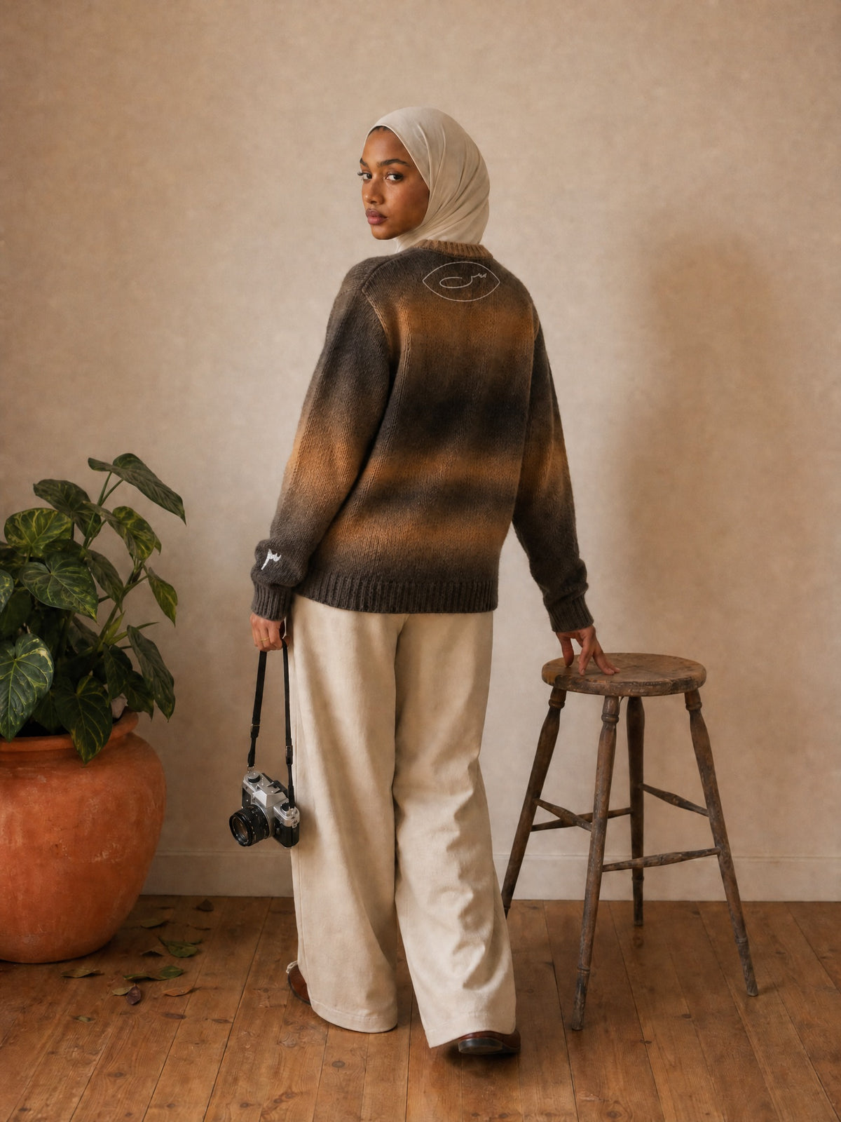 Amina im SYRVAIN «حرا» Strickpullover Braun im Studio, Rückseite mit س-Symbol